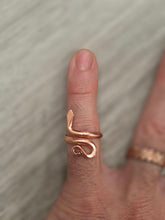 Load image into Gallery viewer, A close-up of a hand wearing a Pure Copper snake wrap ring on the pinky finger, with a blurred second ring on another finger in the background.
