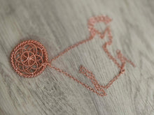 Load image into Gallery viewer, A rose Copper necklace featuring a circular, intricate openwork pendant and a matching link chain, resting on a light gray wood-textured surface.
