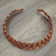 A Pure copper hand woven necklace statement piece displayed on a gray wood-textured surface.