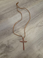 Pure Copper Cross pendant necklace on a light brown cord, laid flat on a gray wood-textured surface.