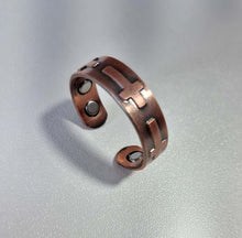 Load image into Gallery viewer, A copper-toned open cuff ring with a geometric cutout pattern and circular magnetic inserts, resting on a textured light gray surface.
