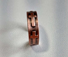 Load image into Gallery viewer, A copper-colored ring featuring two open cross motifs, standing upright on a textured light gray surface.
