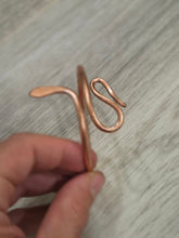 Load image into Gallery viewer, A hand holding a copper wire bangle decorative piece against a light gray wood-grain background.
