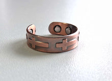 Load image into Gallery viewer, A copper-toned open cuff bracelet with a cross cutout design, resting on a white textured surface.
