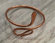 Load image into Gallery viewer, A handmade copper wire open ring bangle with a textured, hammered finish, resting on a light gray wood-grain surface.
