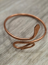 Load image into Gallery viewer, Pure Copper open wrap bangle with a textured finish, resting on a light gray wood-grain surface.
